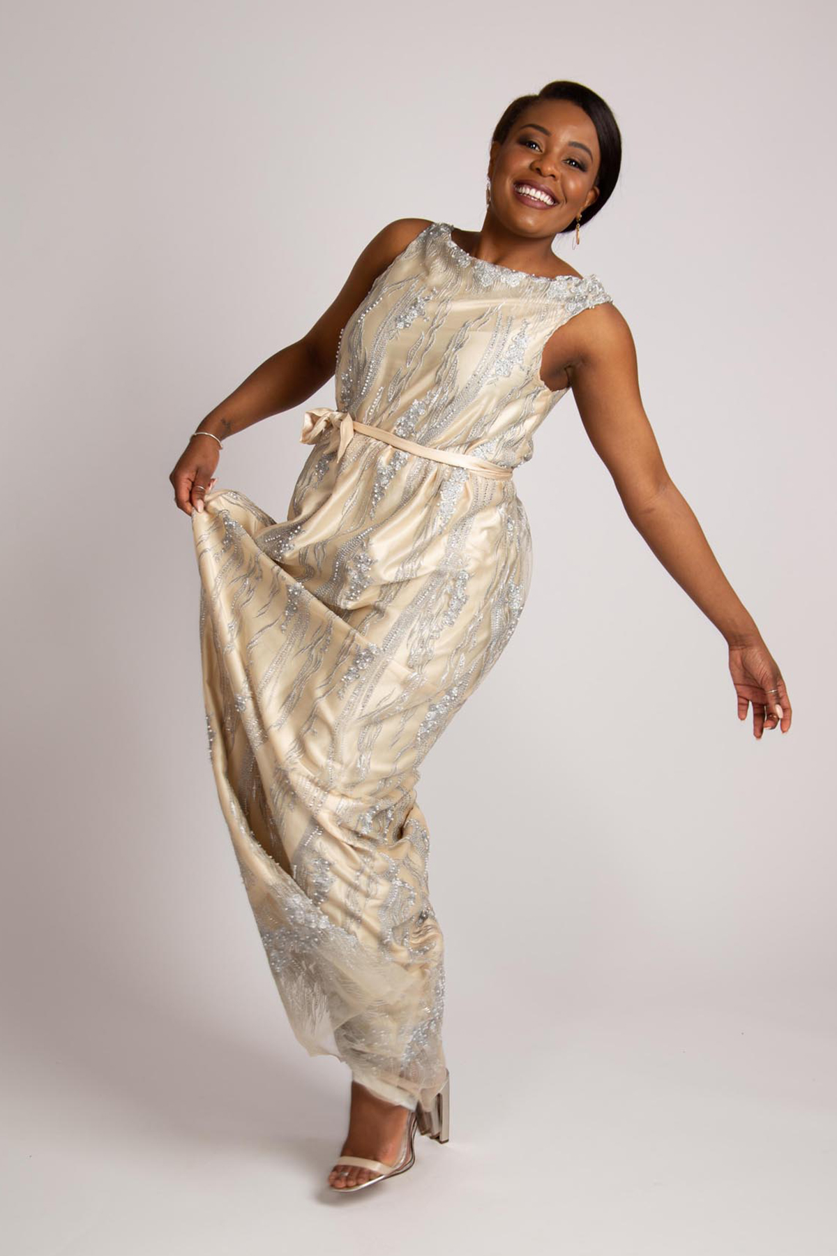 Gabriella Kalema models a pale yellow evening gown with boat neck and ribbon belt made of tulle with embroidery.